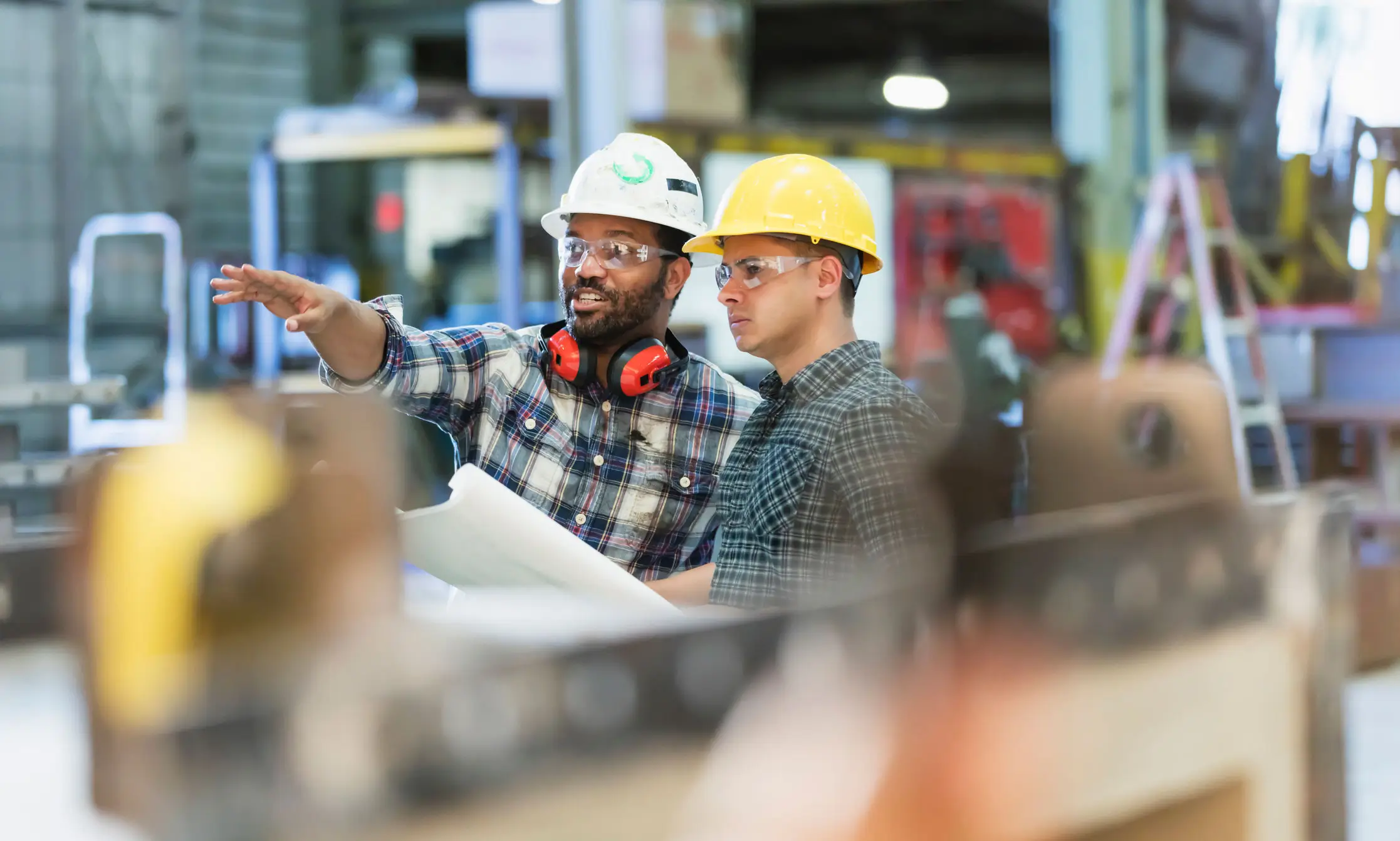 two men in factory looking out at point in distance, one man pointing